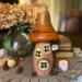 A mushroom fairy house made from dried gourds. It has an orange roof, carved windows, a Rabbit Chateau House sign hangs off the side.